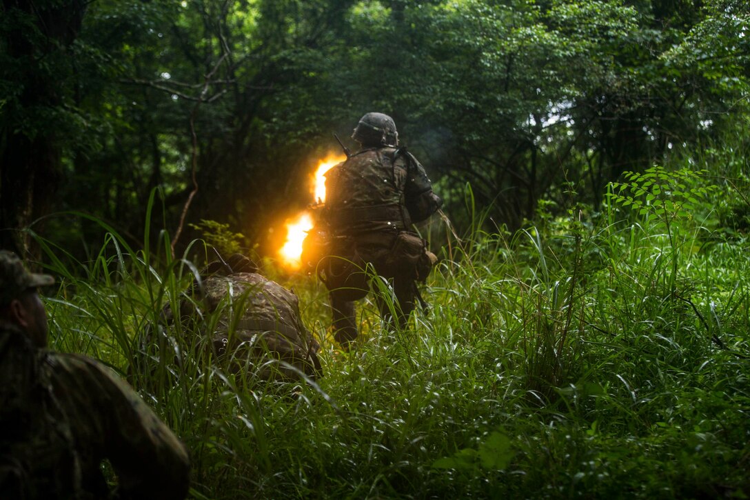 Gunfire is seen as a Marine fires a weapon in the woods.