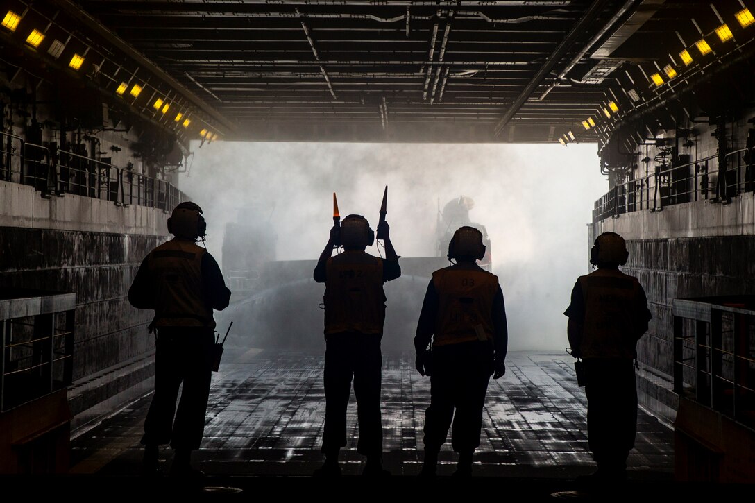 Service members signal to a small boat as it enters a ship.
