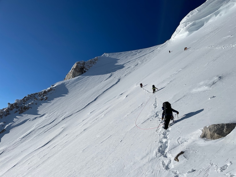 Five climbers hike up a steep snowy mountain.
