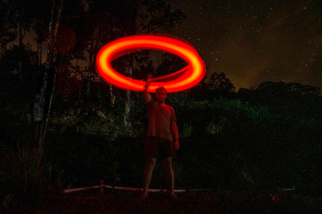 An airman swings a red light stick in a circle over his head at night.