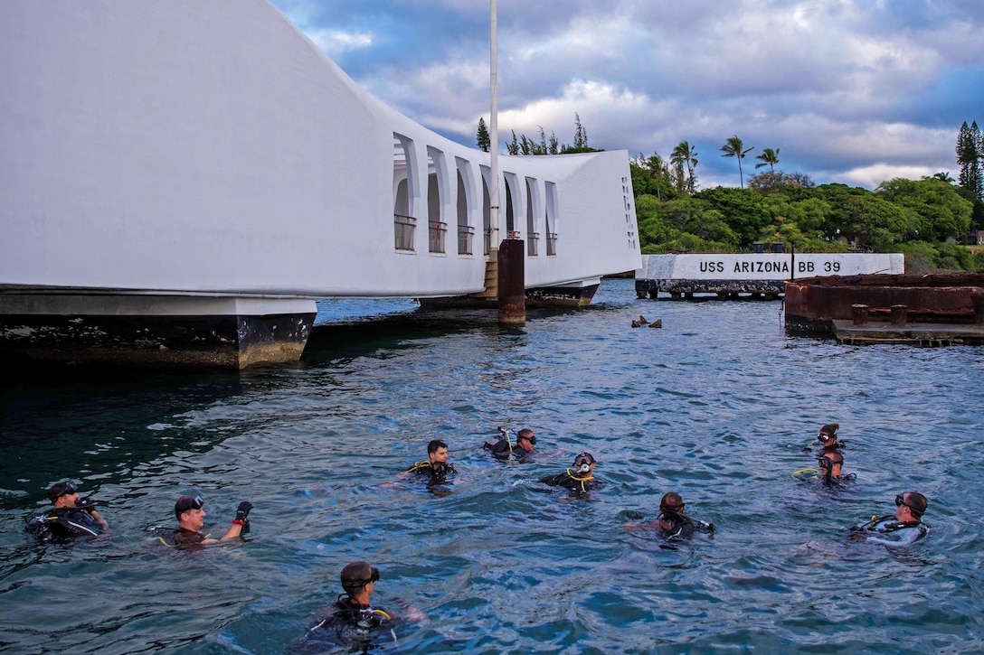 Sailors in dive gear move through water.