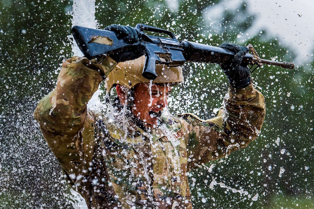 An Air Force cadet holds up a weapon as water falls from above.
