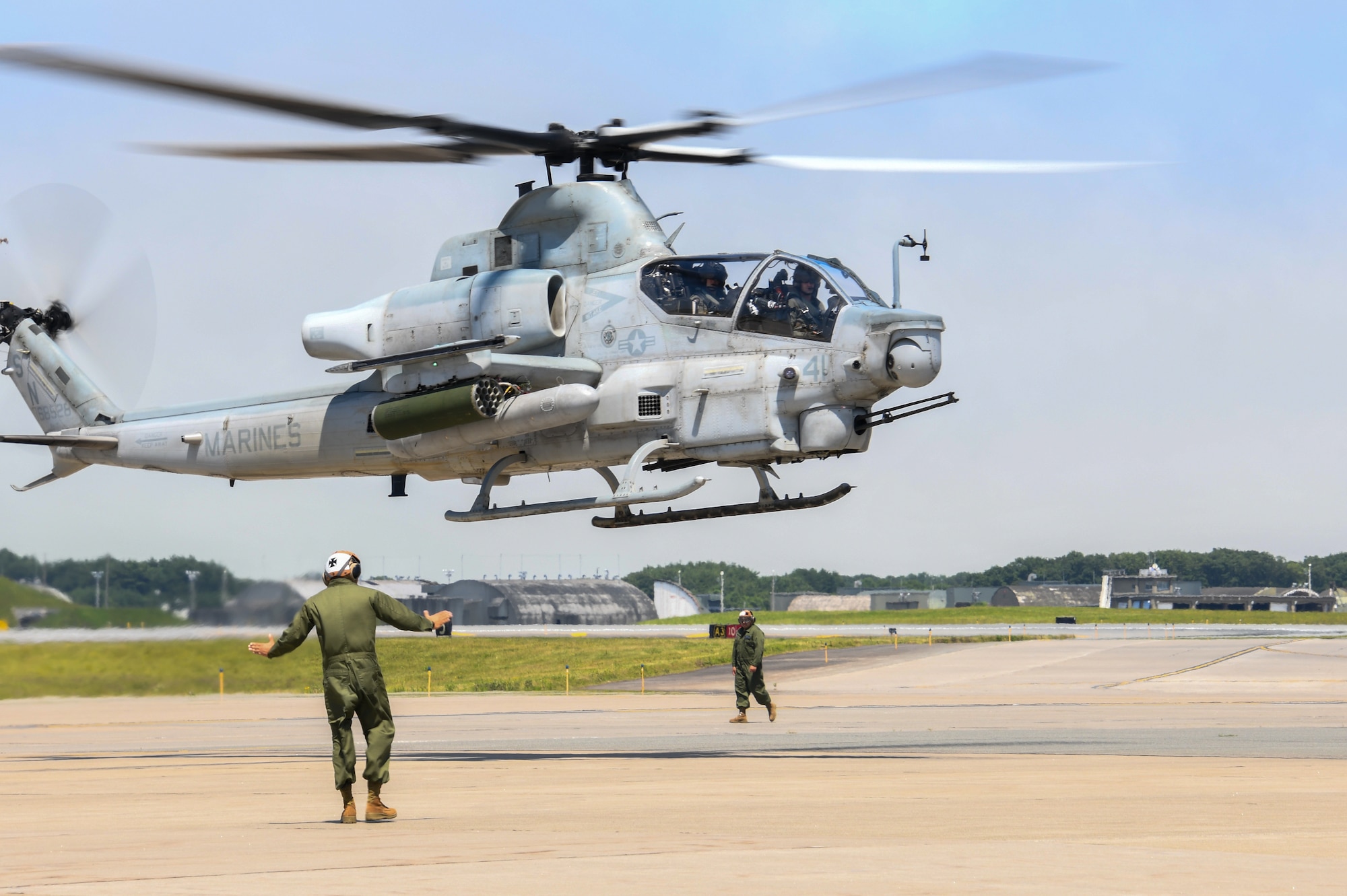 two people in uniform stand on pavement under a hovering helicopter