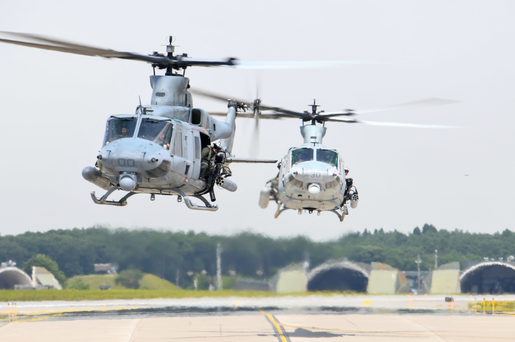 two helicopters fly above an airfield