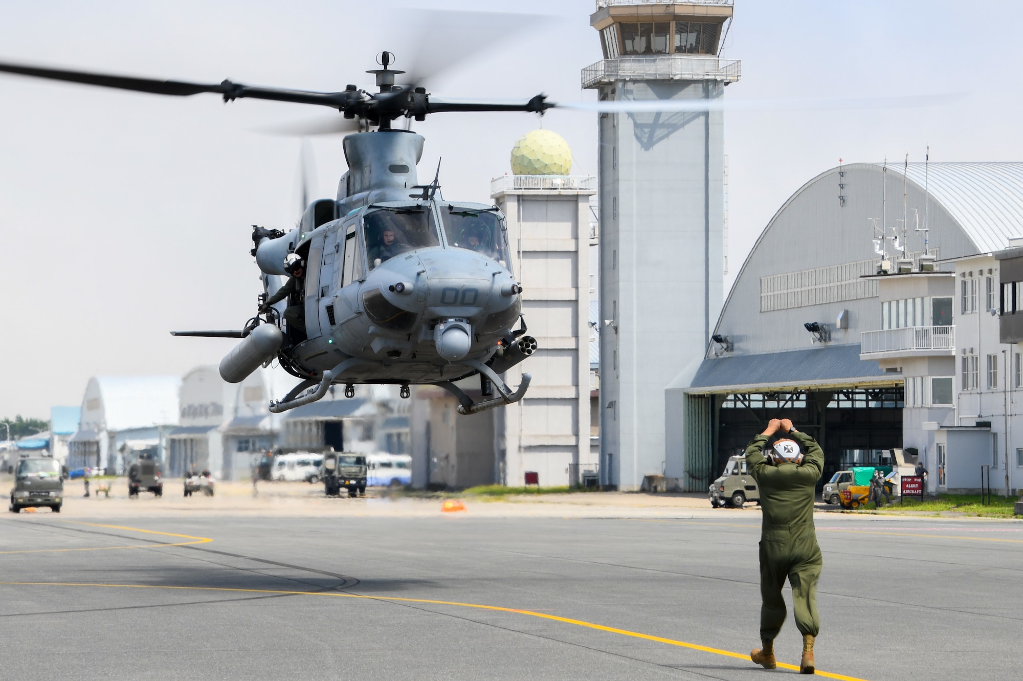 A man in uniform uses hand signals to communicate with a helicopter in flight.