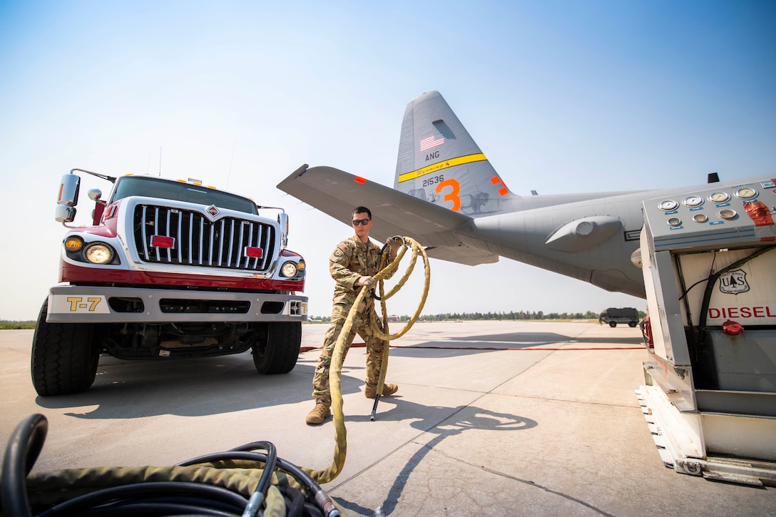 An airman curls up a long yellow hose on the tarmac of an airbase.