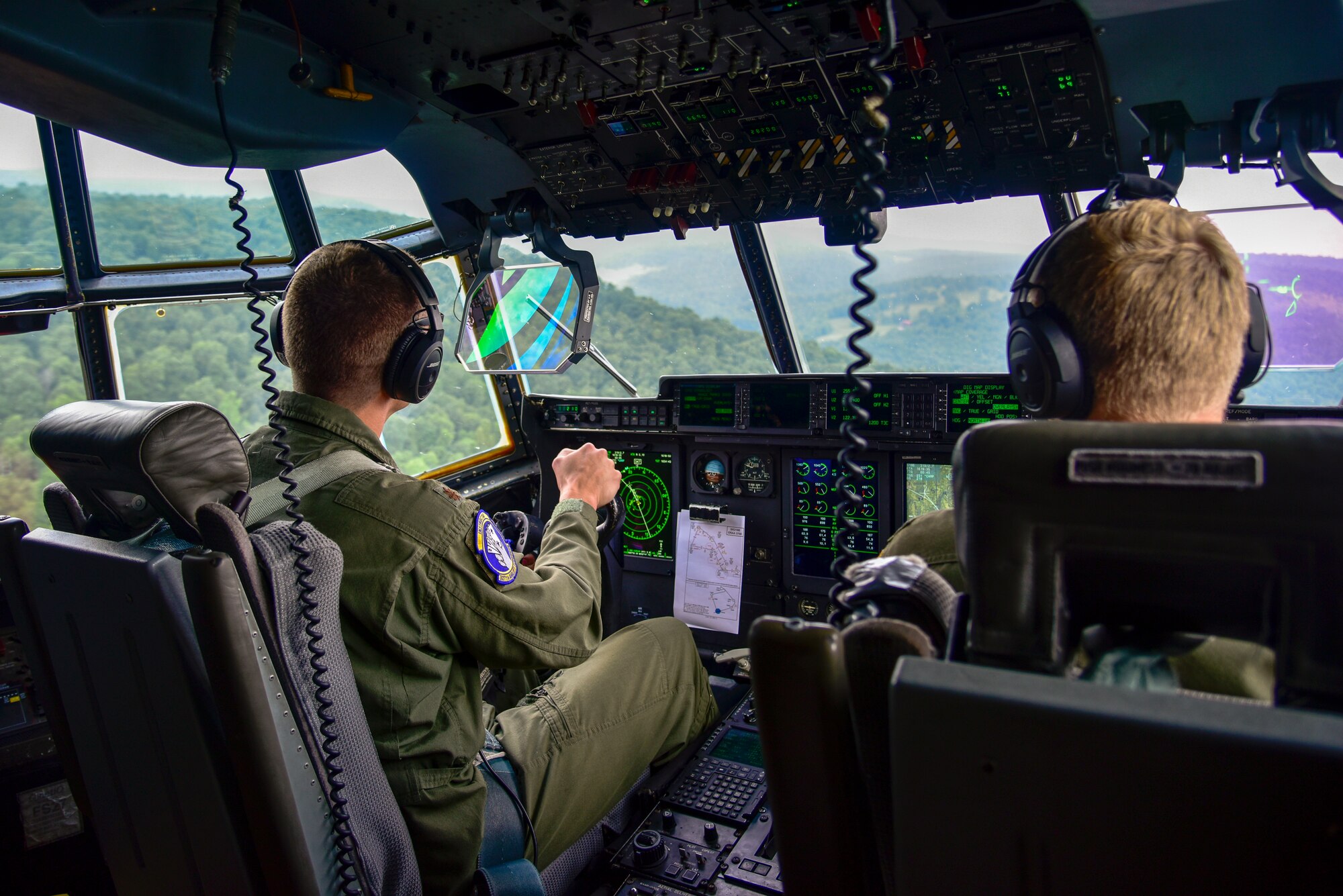 Two pilots in the cockpit flying over terrain.