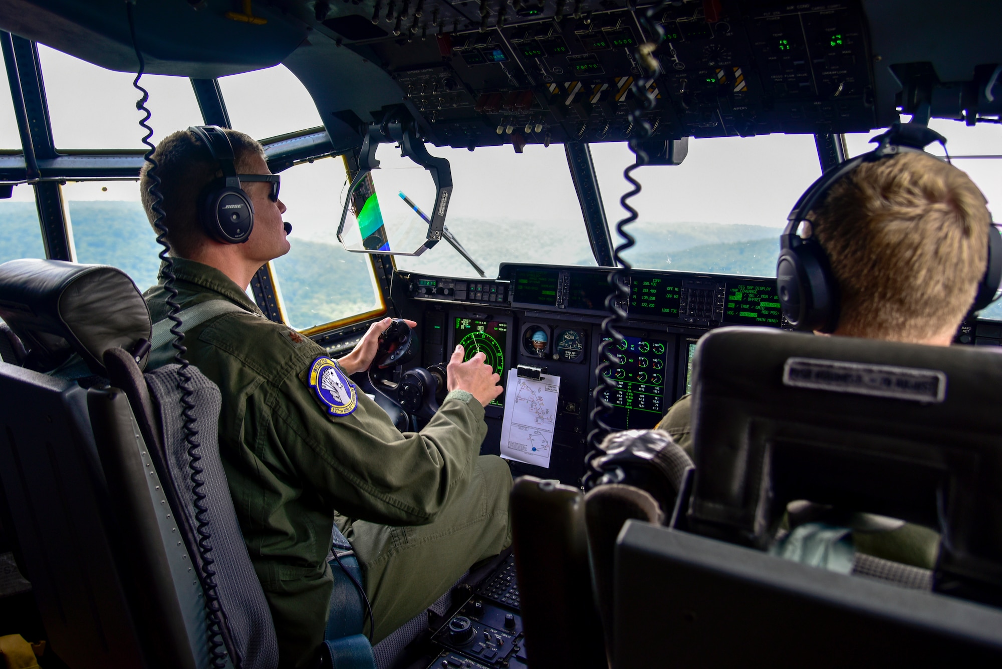 Two pilots in the cockpit flying over terrain.