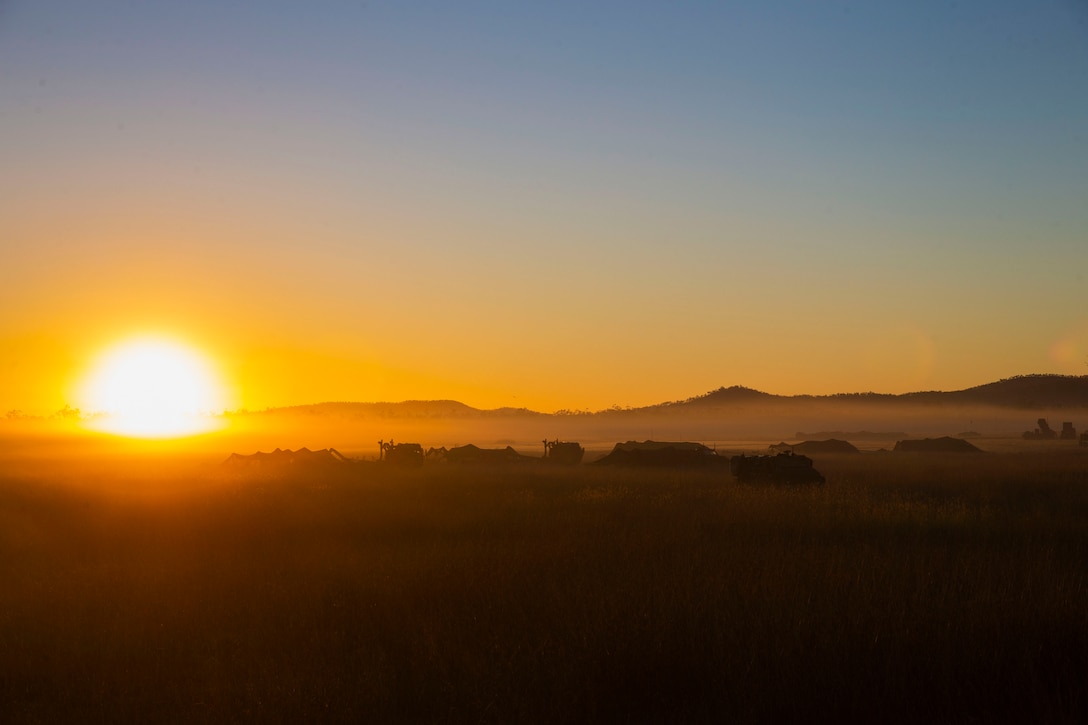 The sun shines on the horizon in a desert terrain.