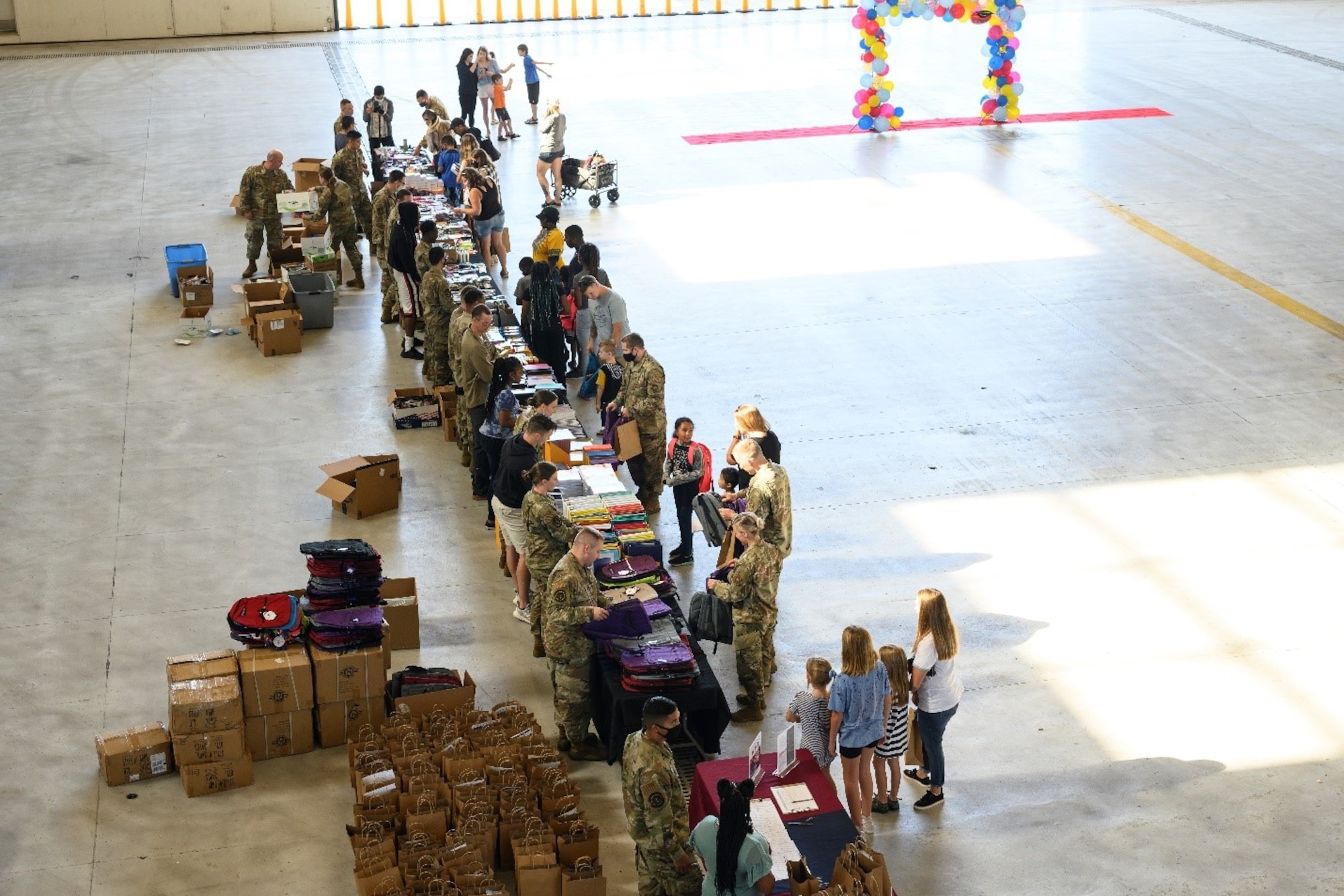Airmen, parents and students line up along a string of tables to look over a selection of free school supplies during the Back-to-School Brigade July 23, 2021, at Travis Air Force Base, California. The school supplies are given away for free as part of the base’s annual tradition of ensuring all returning students have the resources they need ahead of the start of the new school year. (U.S. Air Force photo by Staff Sgt. Christian Conrad)