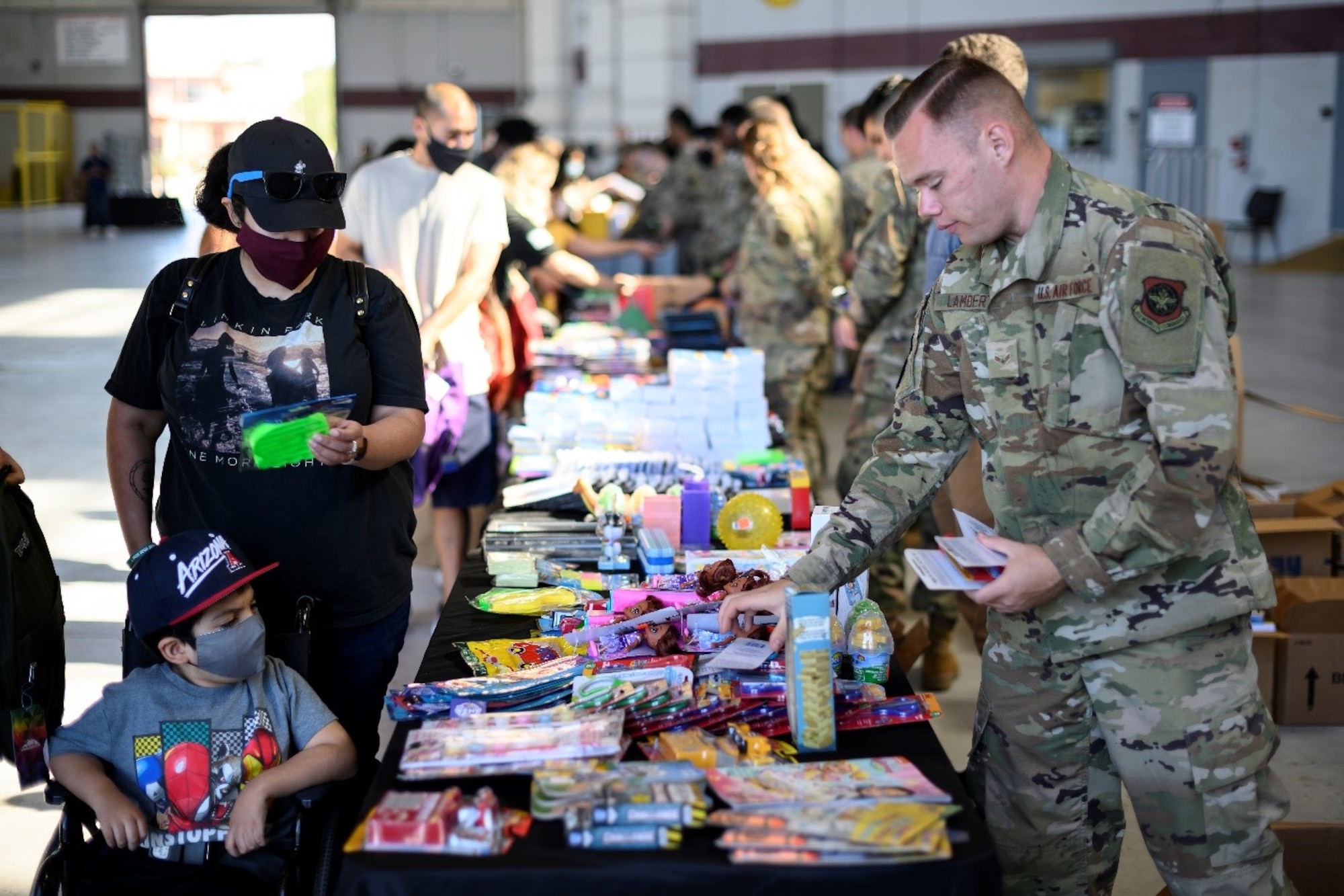 Airmen, parents and students line up along a string of tables to look over a selection of free school supplies during the Back-to-School Brigade July 23, 2021, at Travis Air Force Base, California. The school supplies are given away for free as part of the base’s annual tradition of ensuring all returning students have the resources they need ahead of the start of the new school year. (U.S. Air Force photo by Staff Sgt. Christian Conrad)