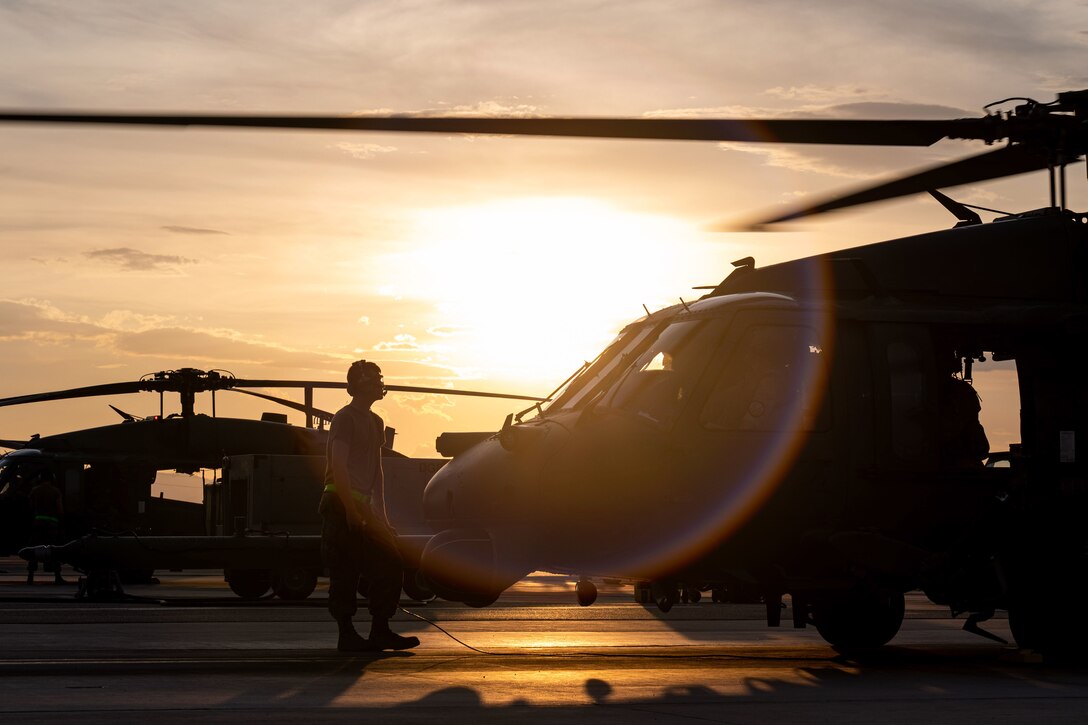 An airman stands next to two aircraft in silhouette.