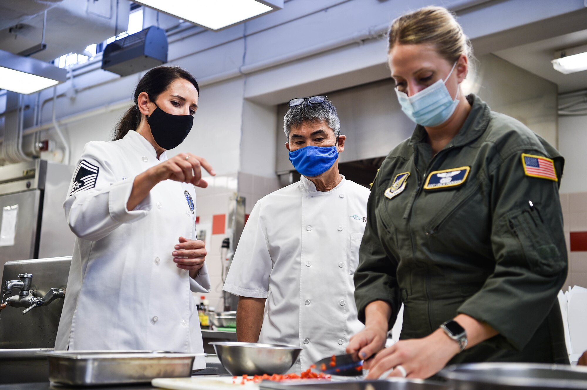 Senior Master Sgt. Jennifer Medeiros, Pacific Air Forces enlisted aid regional manager, speaks with celebrity chef, Roy Yamaguchi, while Staff Sgt. Leslie Frederick, 65th Airlift Squadron flight attendant, prepares a bell pepper at Joint Base Pearl Harbor-Hickam, Hawaii, July 21, 2021. Yamaguchi observed culinary skills Airmen and Sailors have acquired during their time in service. (U.S. Air Force photo by Senior Airman Alan Ricker)
