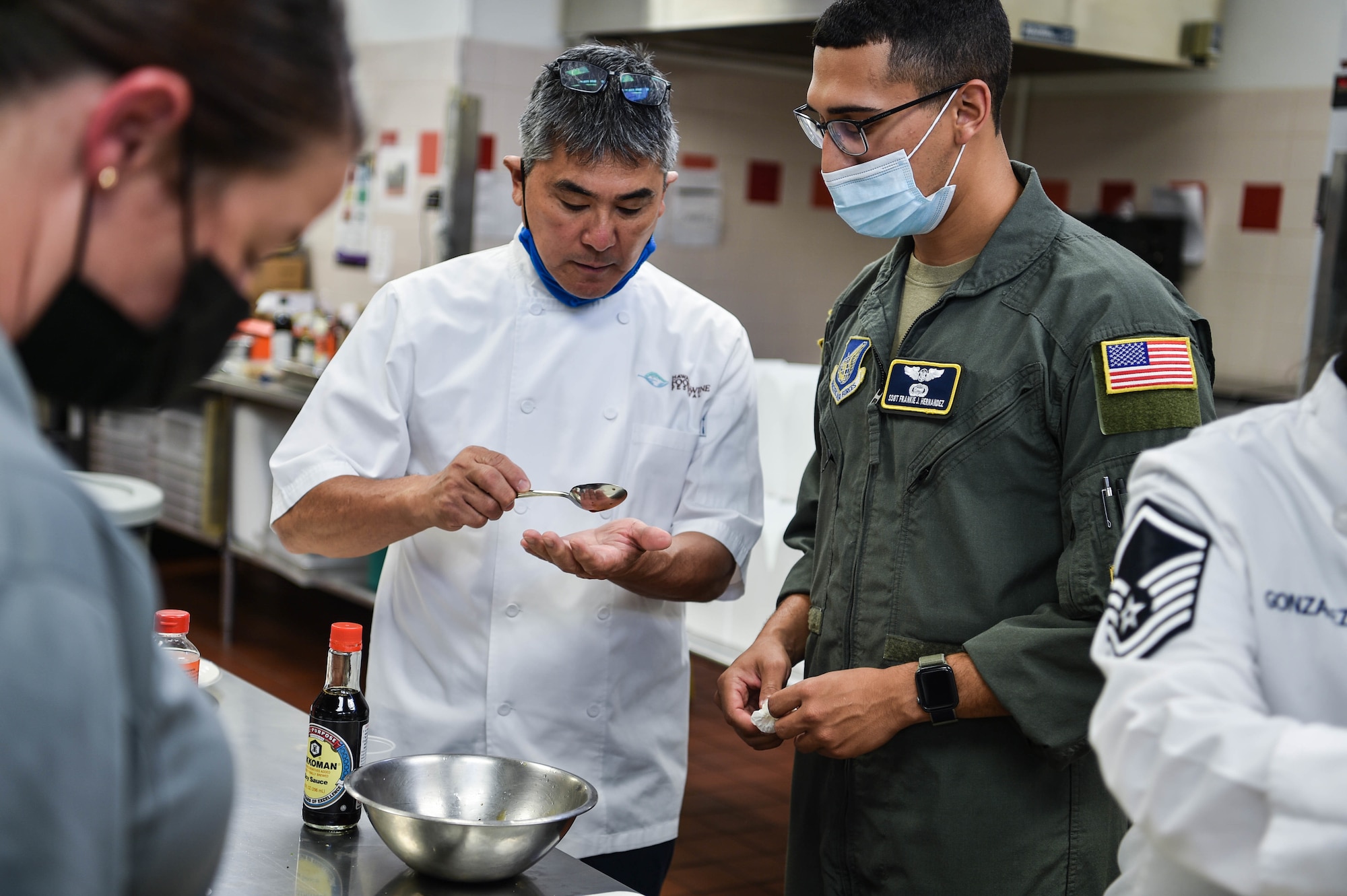 Celebrity chef, Roy Yamaguchi, tastes a sauce created by Staff Sgt. Frankie Hernandez, 65th Airlift Squadron flight attendant, during his visit to the Hale Aina Dining Facility at Joint Base Pearl Harbor-Hickam, Hawaii, July 21, 2021. Three teams, combined of Airmen and Sailors, were challenged to present a dish to Yamaguchi within an hour, testing their teamwork and culinary skills. (U.S. Air Force photo by Senior Airman Alan Ricker)