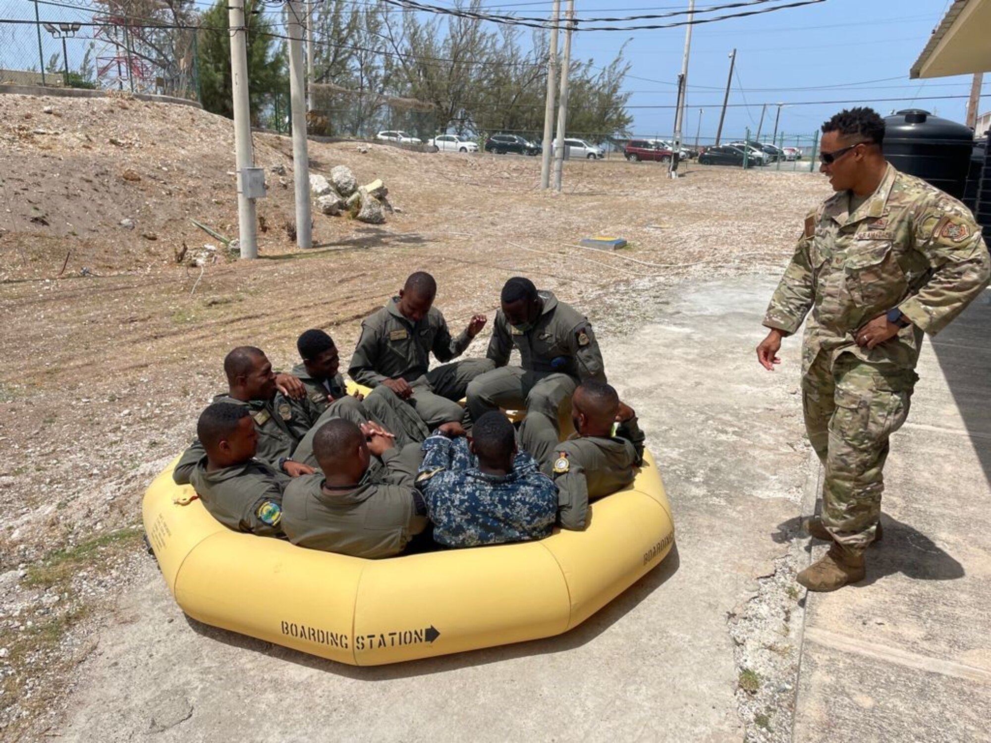 U.S. Air Force Tech. Sgt. Gerame Vaden, 571st Mobility Support Advisory Squadron air advisor, instructs Jamaican Defense Force Air Wing aircrewmen on life raft inflation and embarkation on land prior to moving to the water June 16, 2021, at the Caribbean Military Aviation School, Kingston, Jamaica.  Air advisors train and assist partner nations in developing air mobility capabilities through Mobile Training Team engagements. (Courtesy photo)