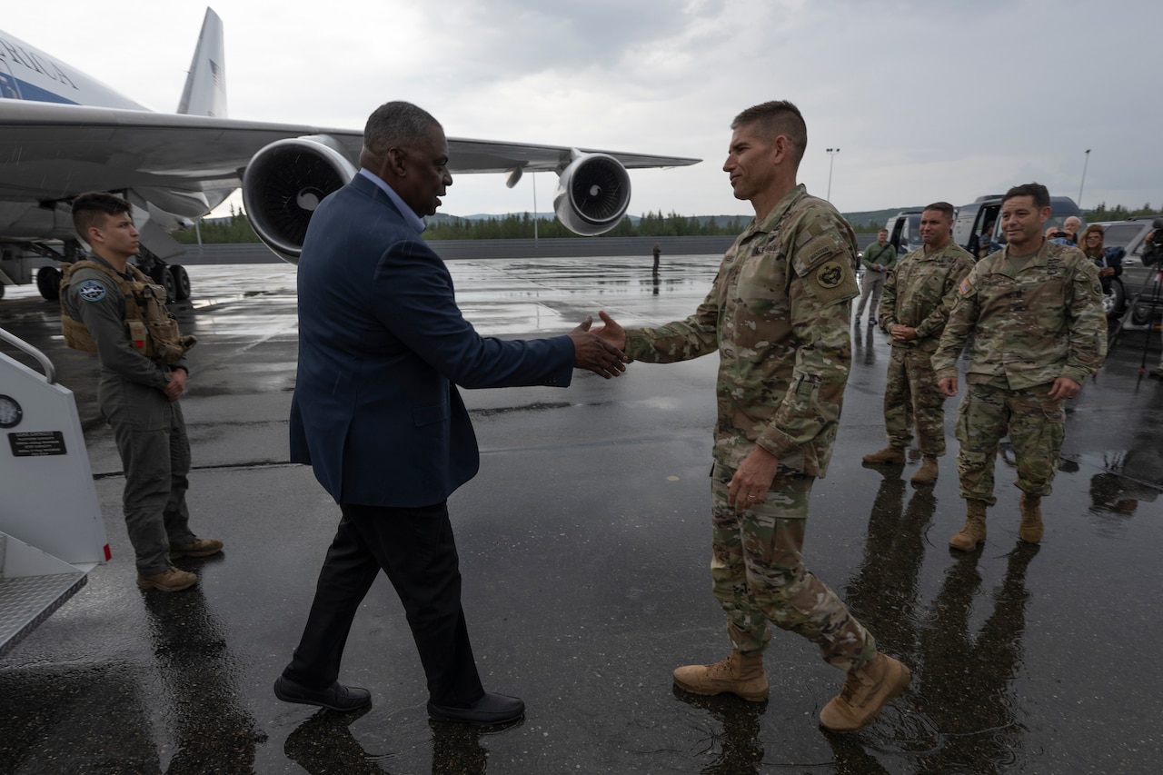 Two man shake hands as others stand around.