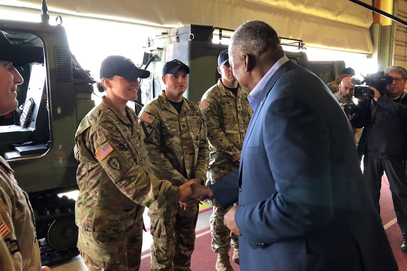 A man shakes the hand of a service member as other watch.