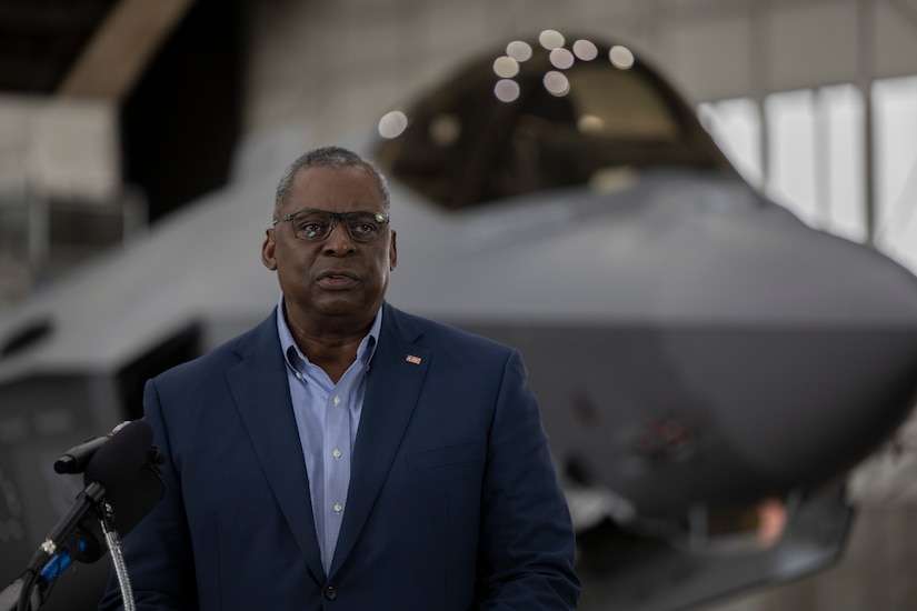 Secretary of Defense Lloyd Austin stands in front of a microphone.