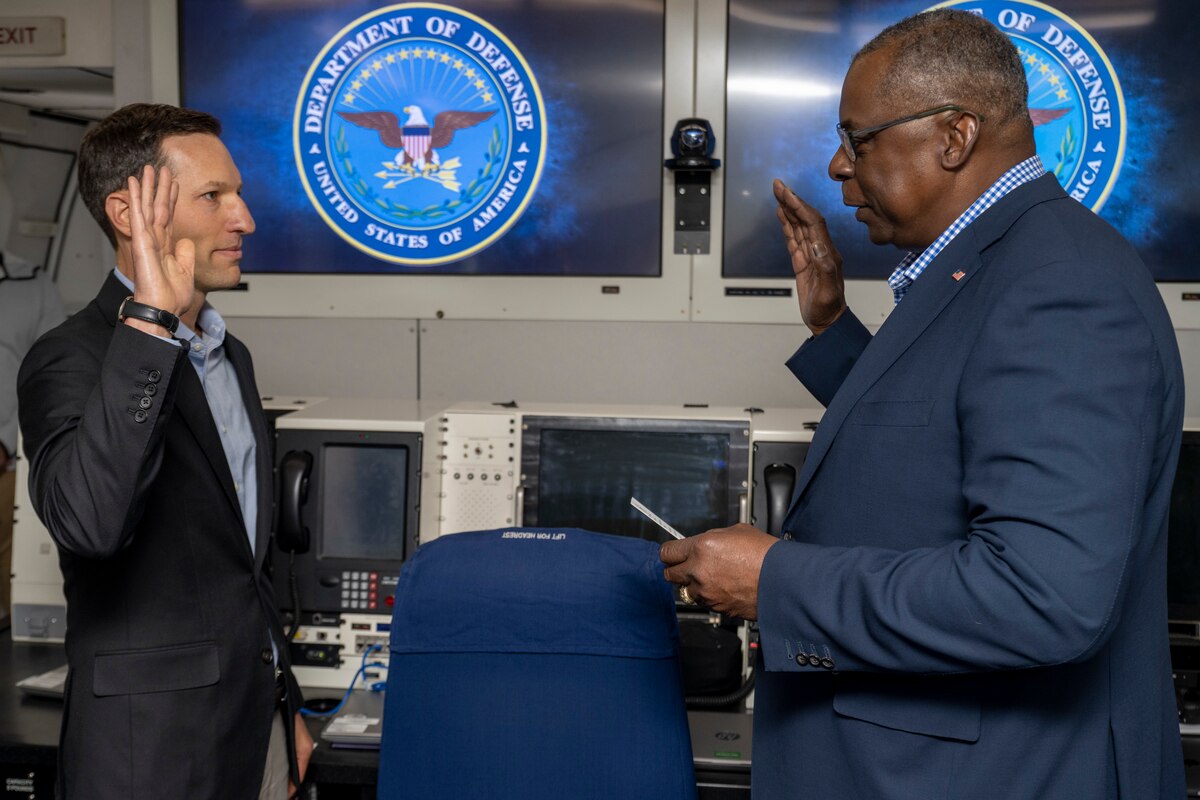 Two men face one another; both hold up their right hands.