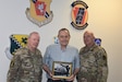 Richard Posey, center, son of Pennsylvania’s first Deputy Adjutant General for Air, Brig. Gen. Richard Posey, holds a photo of his father while standing with current DAG-A, Brig. Gen. Michael Regan, left, and state Command Chief Paul Frisco, right, in front of the shields representing Pennsylvania Air National Guard Headquarters and each of the state’s three Air National Guard Wings.