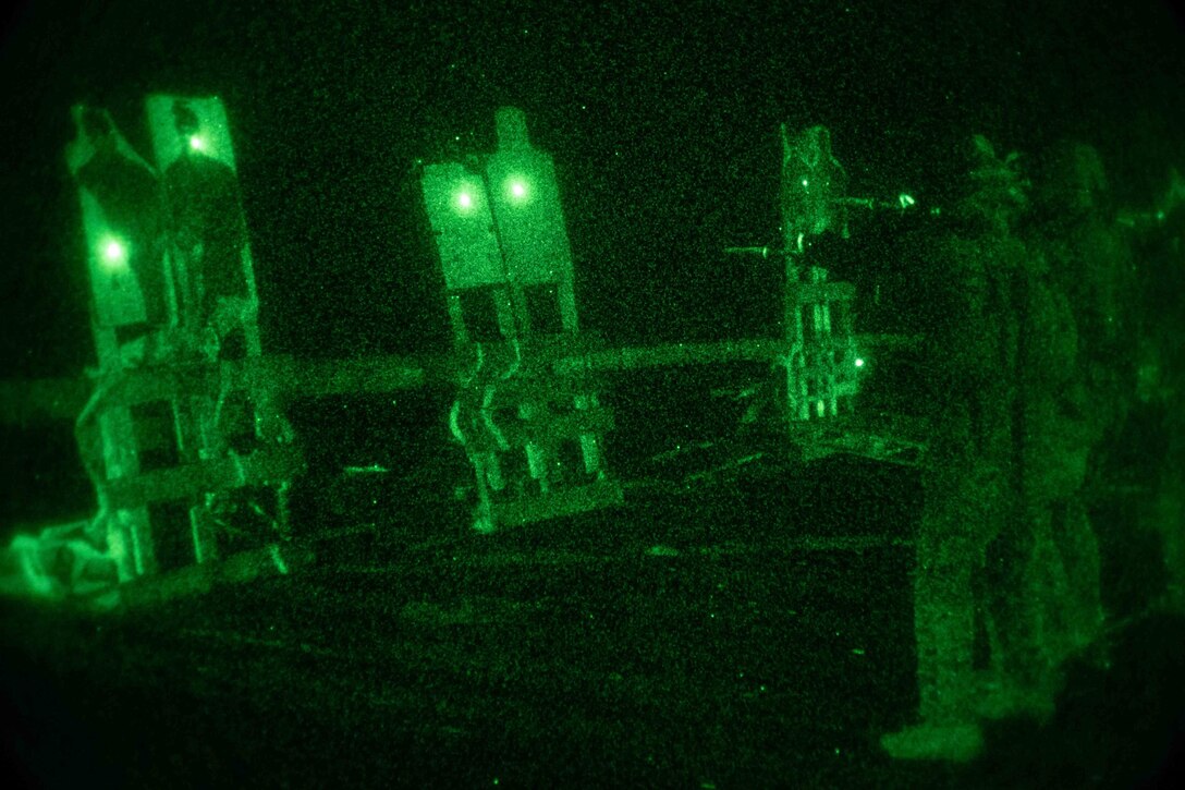 Marines fire at targets under a green light at night.