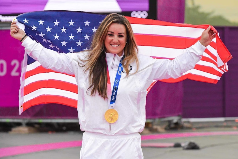 A female athlete smiles as holds the American flag.