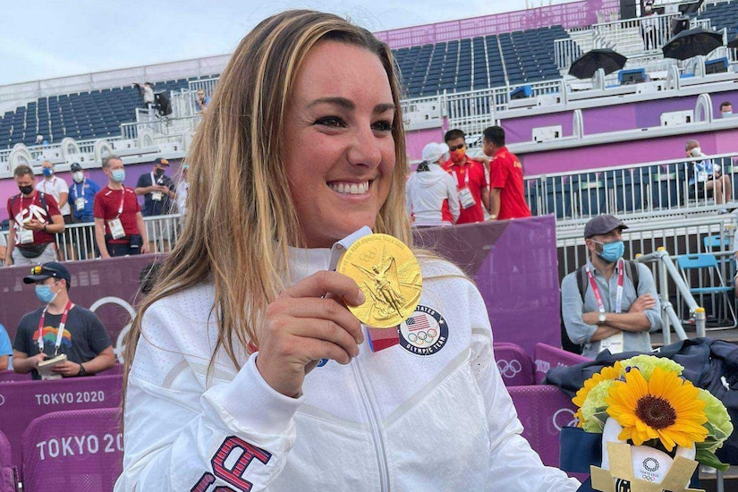 A female athlete smiles as hold a gold medal in her hand.