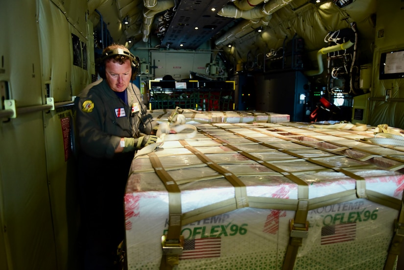A man looks at a large shipment in the cargo hold of a plane.