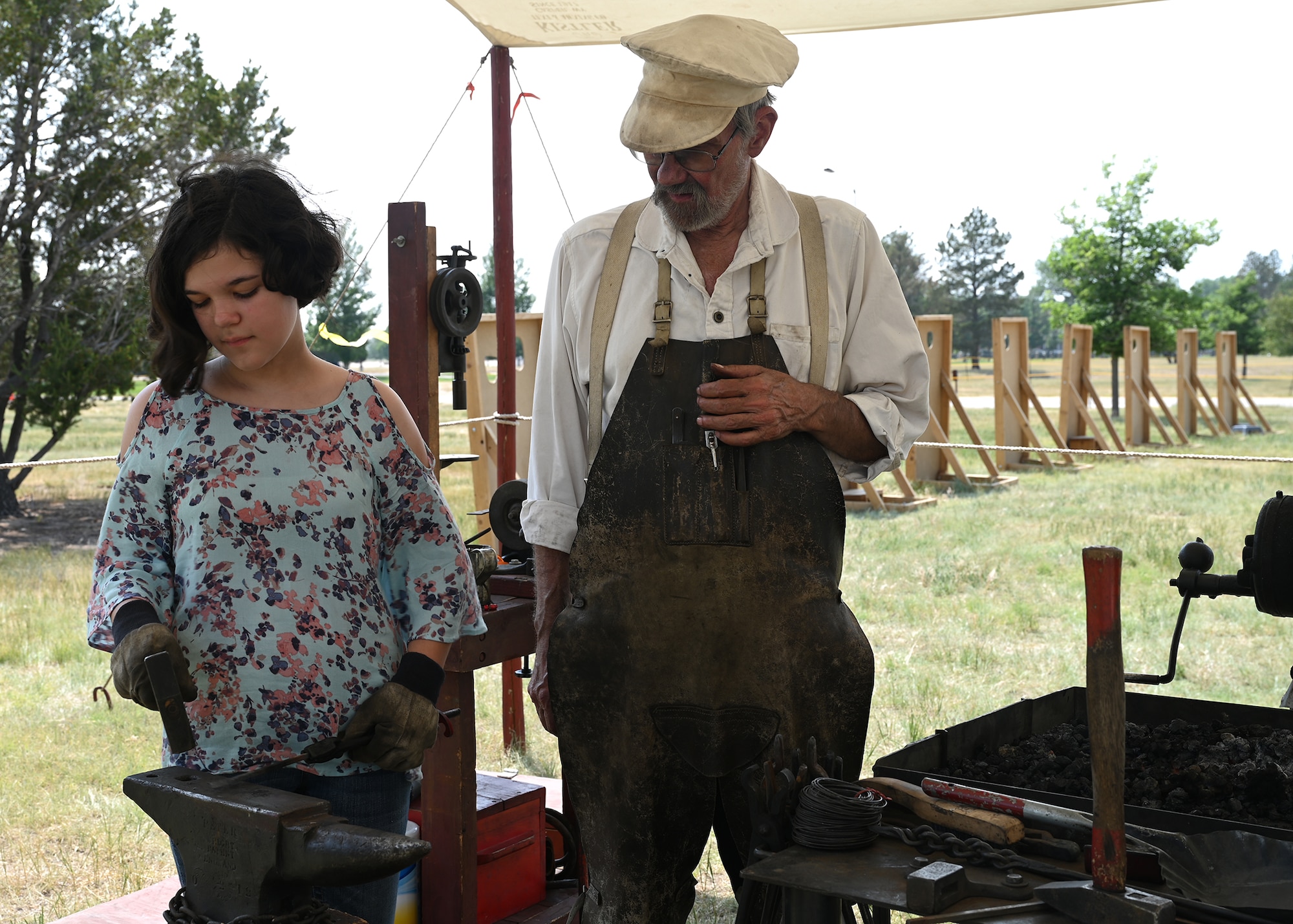 Jeanette Thomas, visitor to Fort D.A. Russell Days, attempts smithing an S-hook under the watchful eye of Jan Manning during the event July 25, 2021, on F.E. Warren Air Force Base, Wyoming. Fort D.A. Russell Days is a time for F.E. Warren Air Force Base to share its history and heritage with the community. (U. S. Air Force photo by Glenn S. Robertson)