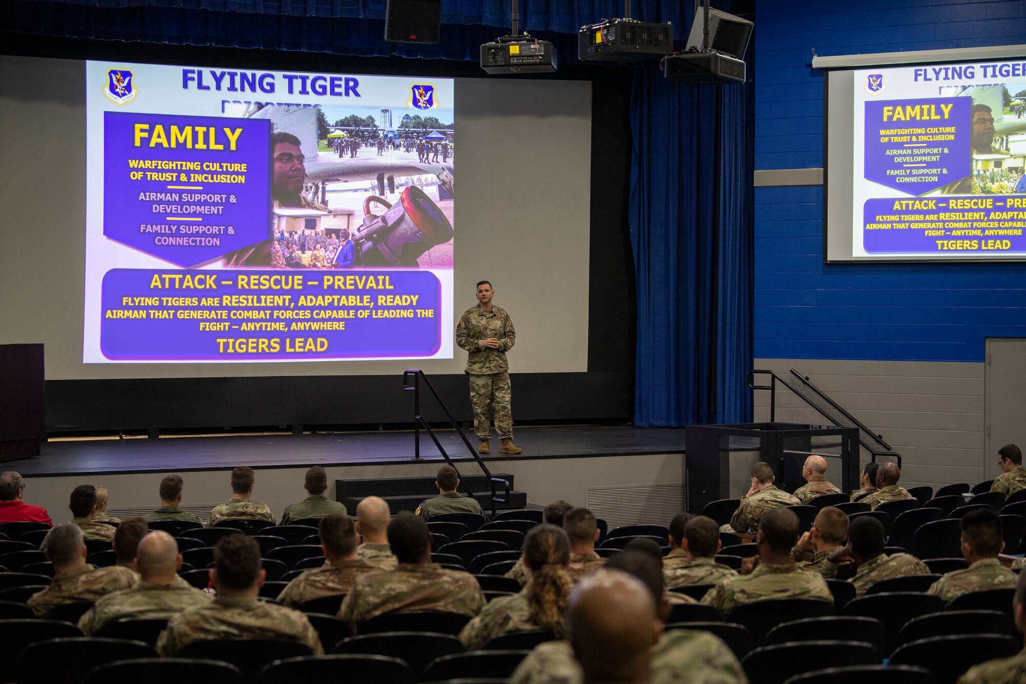 A photo of an Airmen standing on stage in front of a crowd in an auditorium.