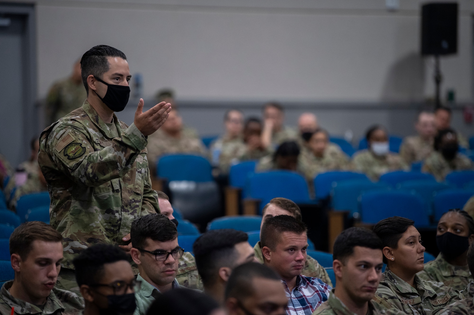 A photo of an Airmen standing in an auditorium with his hand up.