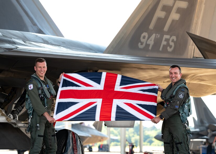 Royal Air Force Squadron Leader Alexander “Thorney” Thorne, departing 94th Fighter Squadron Foreign Exchange Officer, and RAF Squadron Leader David Wild, incoming 94th Fighter Squadron foreign exchange officer, pose for a photo while holding the United Kingdom flag at Joint Base-Langley Eustis June 15, 2021. Wild will take over as Langley’s newest Foreign Exchange Officer and be stationed with the 94th Fighter Squadron for the next three years.