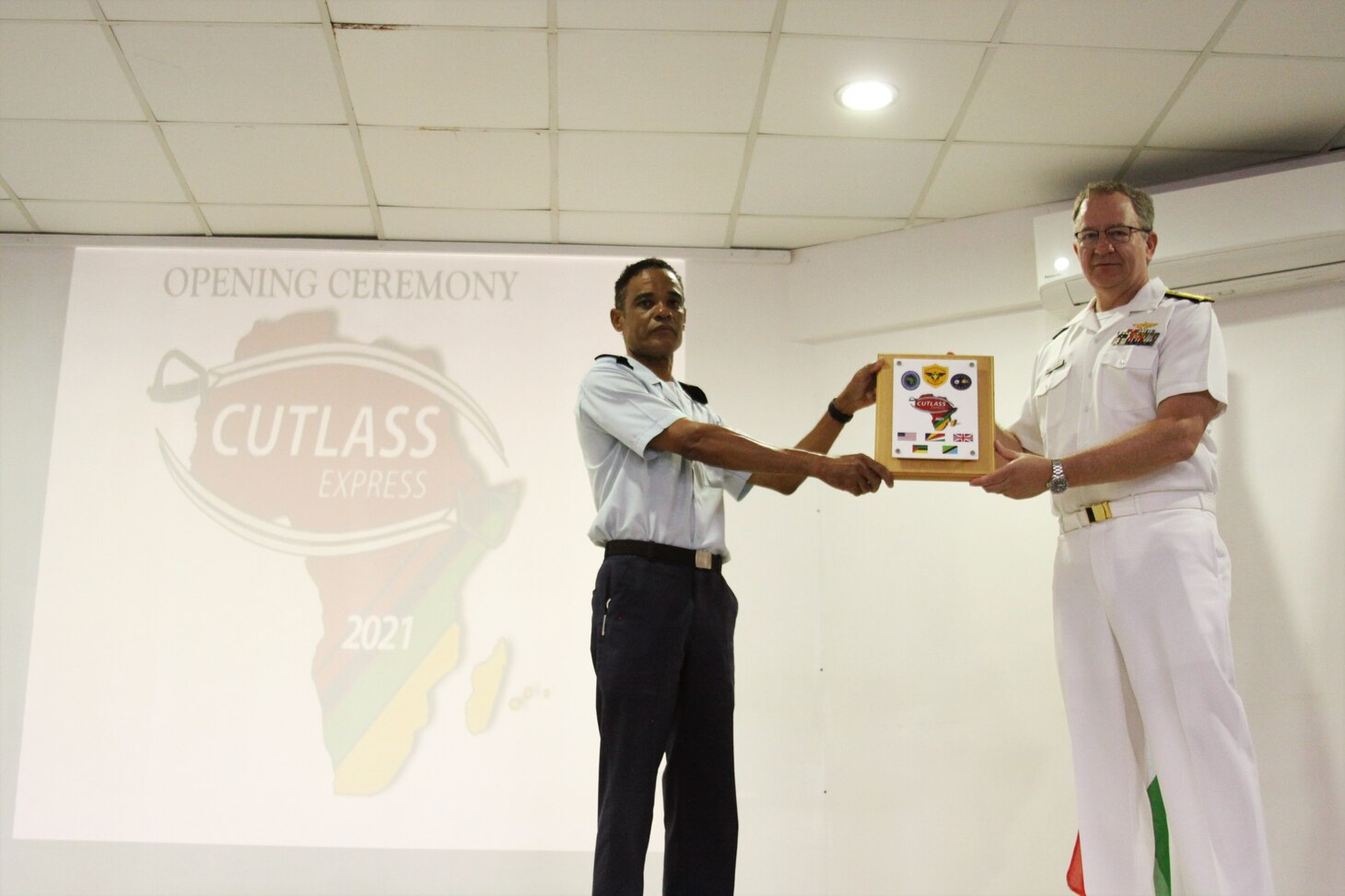 (July 26, 2021) Lt. Col. Jean Attala, Commander, Seychelles Coast Guard, left, exchanges gifts with Rear Adm. Jeffrey Spivey, Director, Maritime Partnership Program, U.S. Naval Force Europe-Africa, U.S. Sixth Fleet, during the opening ceremony of exercise Cutlass Express 2021 held at the Seychelles Coast Guard Academy in Victoria, Seychelles, July 26, 2021. Cutlass Express is designed to improve regional cooperation, maritime domain awareness and information sharing practices to increase capabilities between the U.S., East African and Western Indian Ocean nations to counter illicit maritime activity.