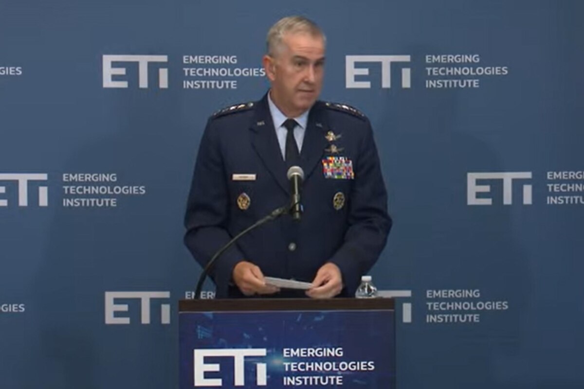 A man in a military uniform stands at a lectern holding a piece of paper.