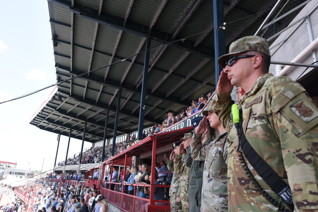 Airmen of the Mighty Ninety salute the flag during its unfurling during Cheyenne Frontier Days Military Monday July 26, 2021, on Frontier Park in Cheyenne, Wyoming. Military Monday honors those serving in the local community and provides an opportunity to showcase the strong relationship between the base and the local community. (U.S. Air Force photo by Maj. Haley Armstrong)