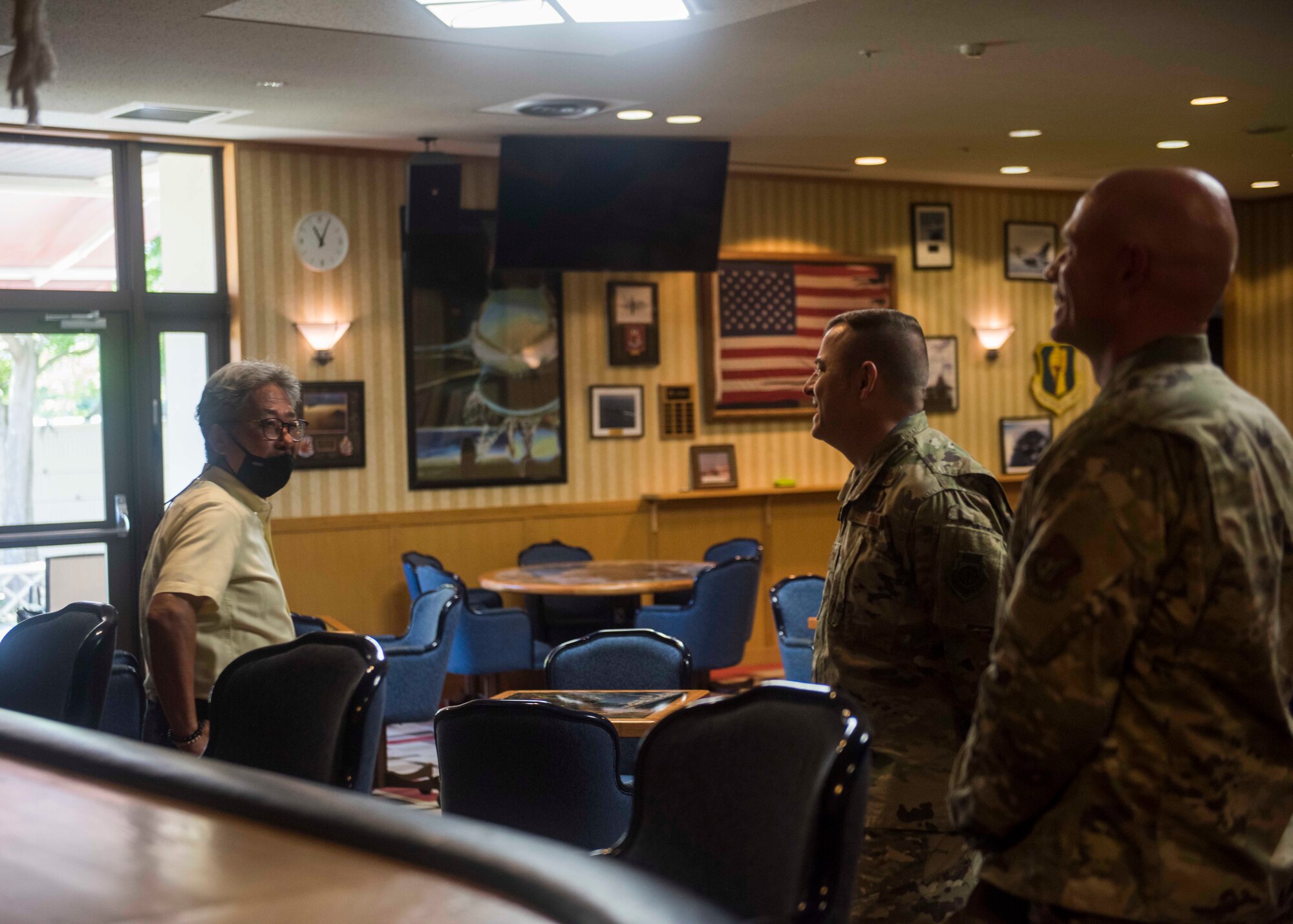 A civilian talks to two service members while standing in a restaurant area.