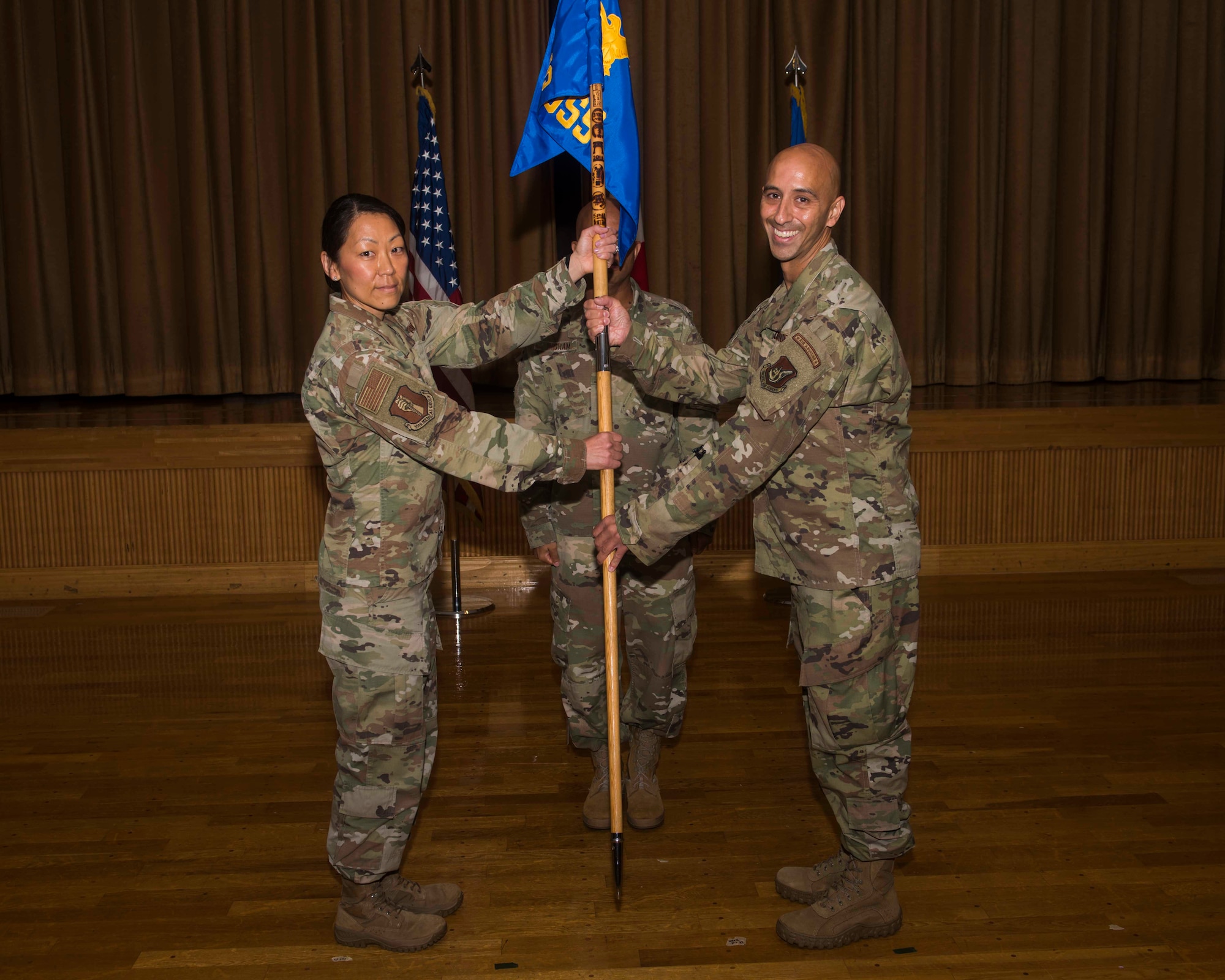 A female service member on the left passes a guidon to a male service member on the right.