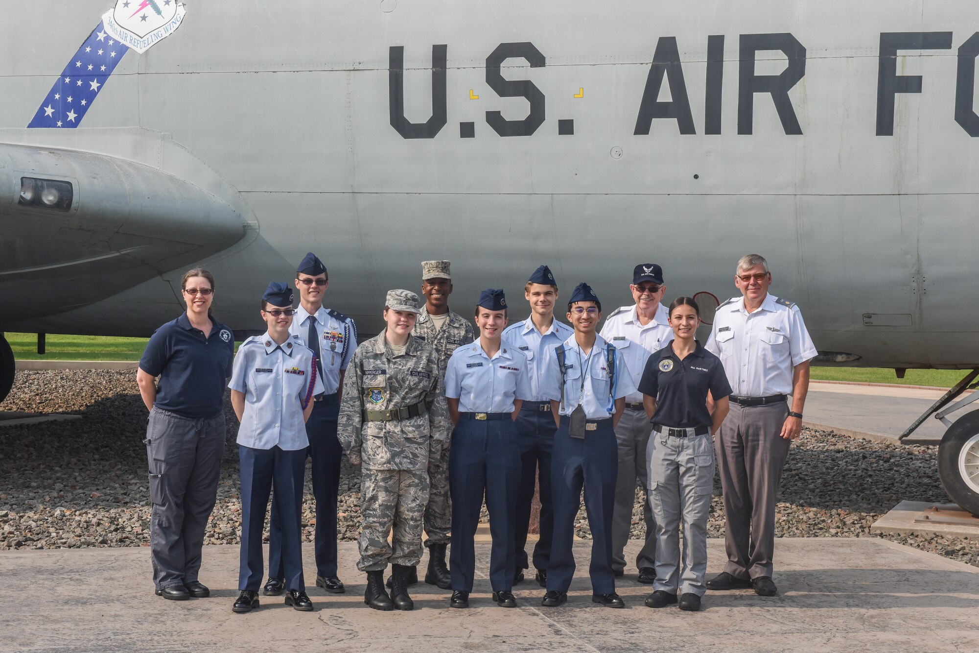 People pose for a group picture in front of an aircraft display