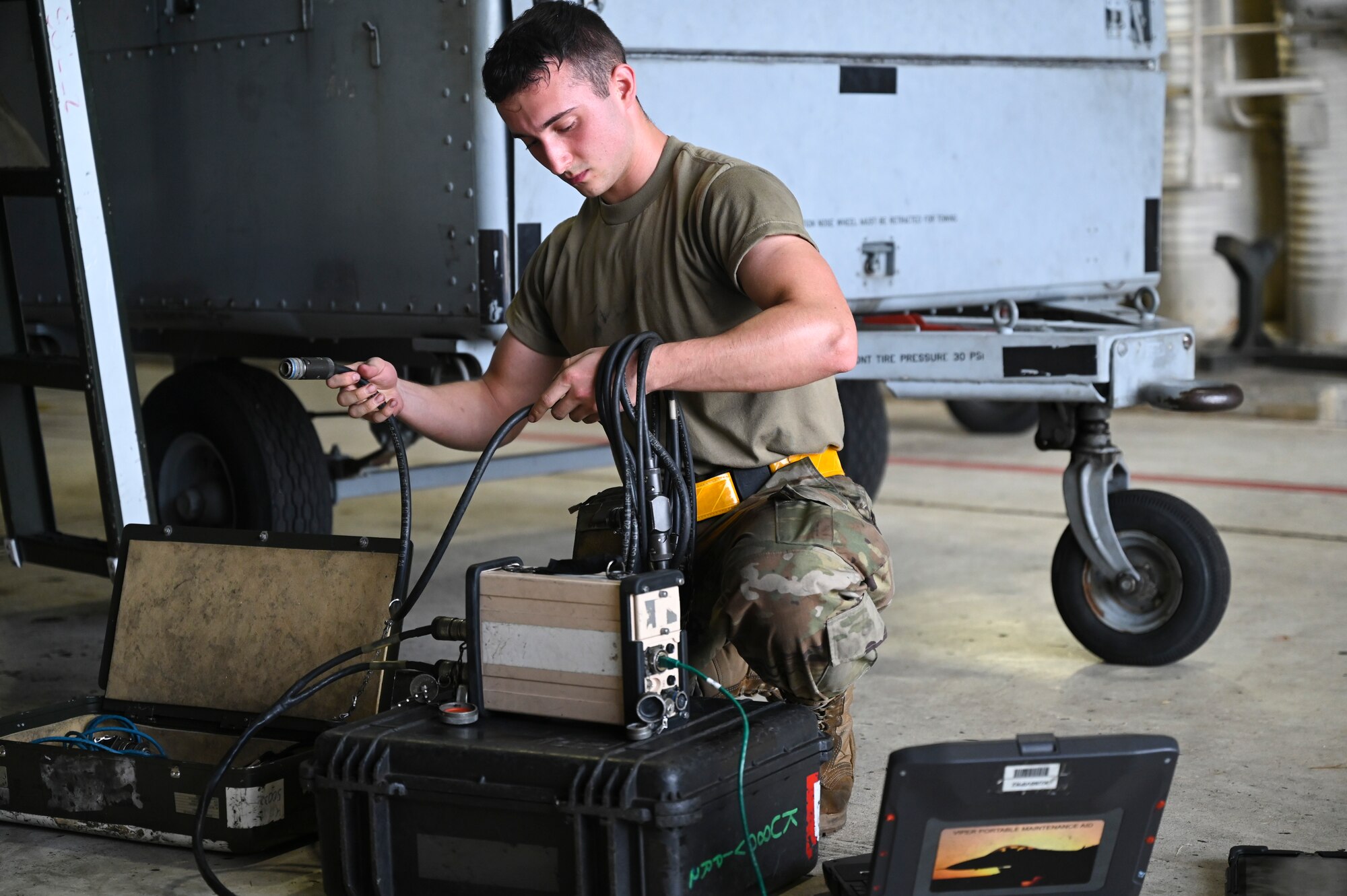 A maintenance Airman sorts through equipment in a hangar.