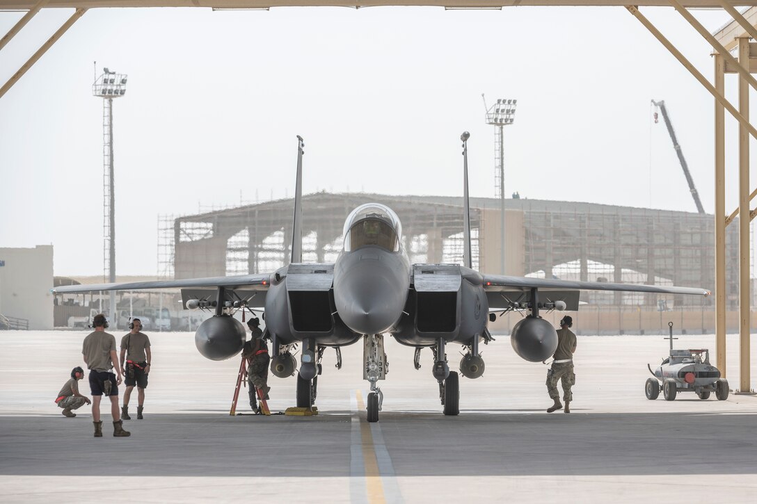 F-15E under a sunshade with maintenance Airmen working around it