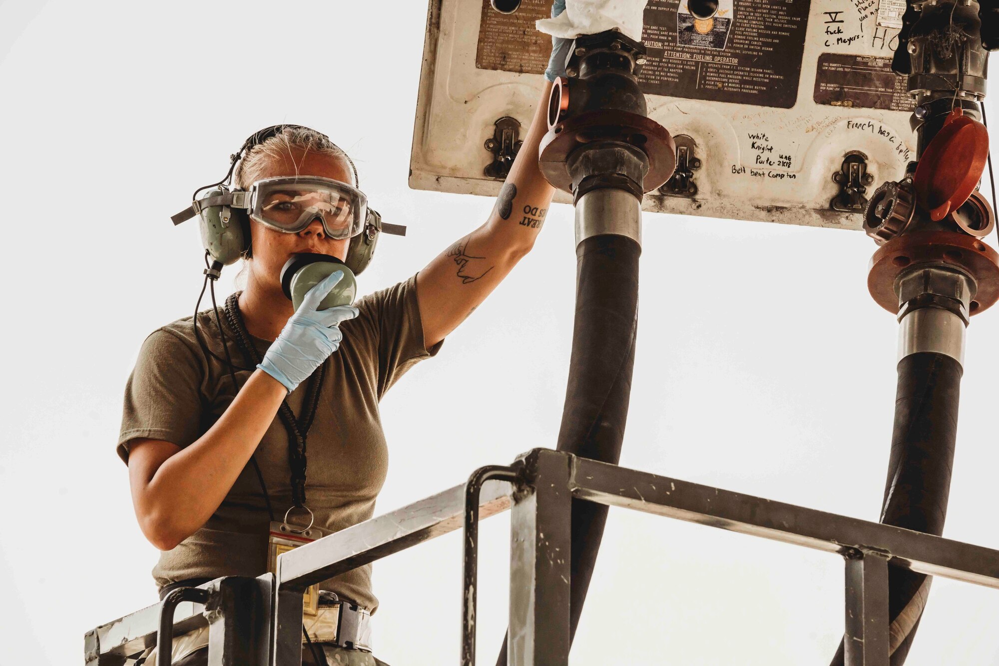 Airman talking on radio and holding fuel hose to an aircraft