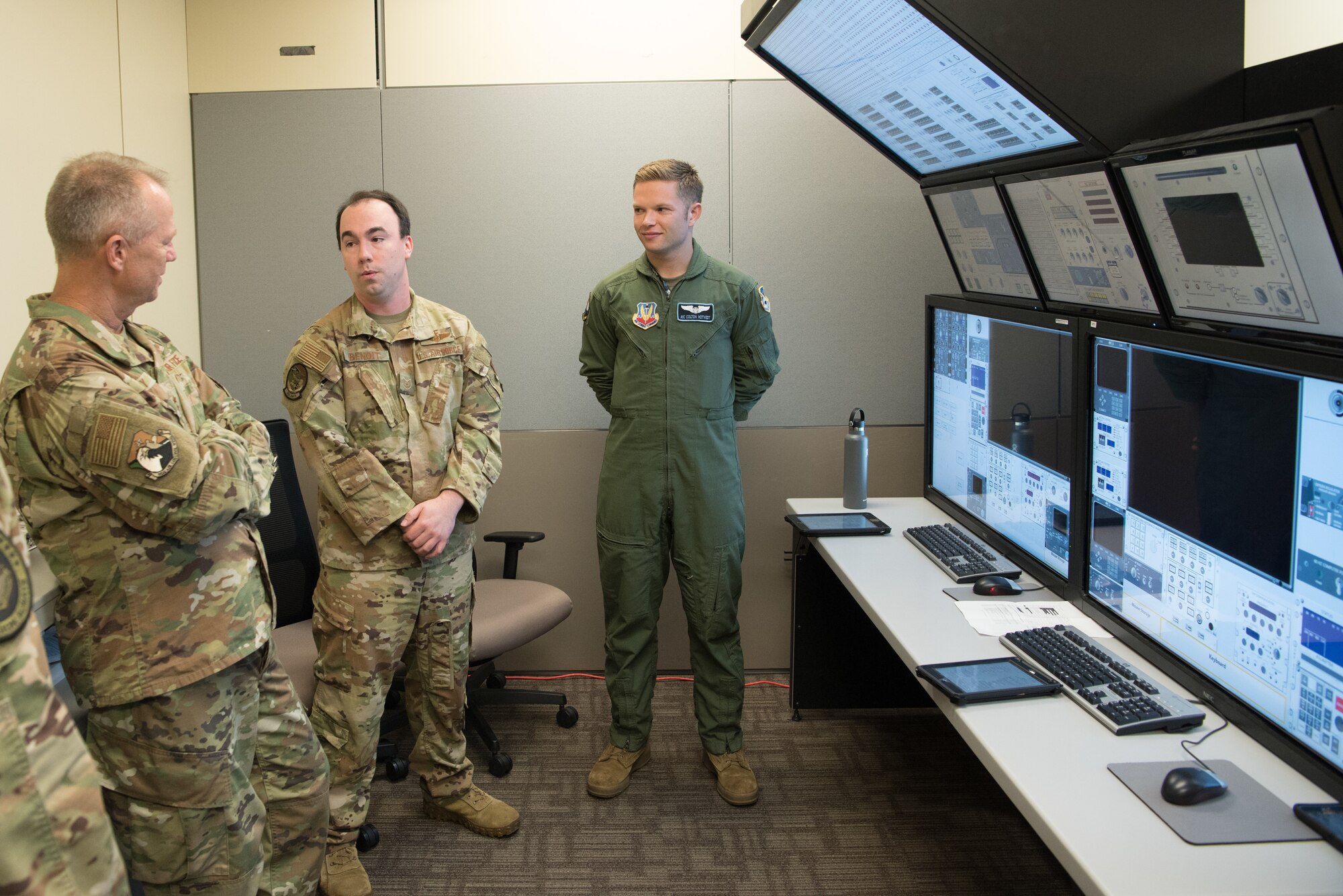 Three men standing in a room with computer screens behind them.