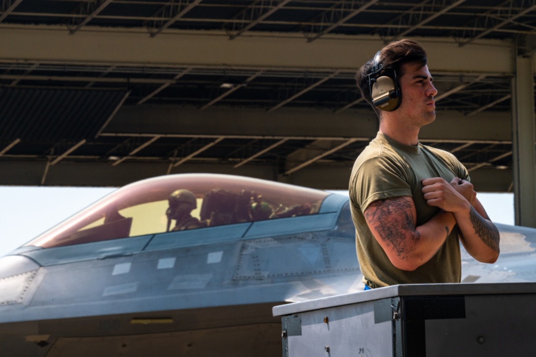 Airman  waits to give the signal to begin taxiing to a F-22 Raptor aircraft at Joint Base Langley-Eustis, Virginia, July 21, 2021.