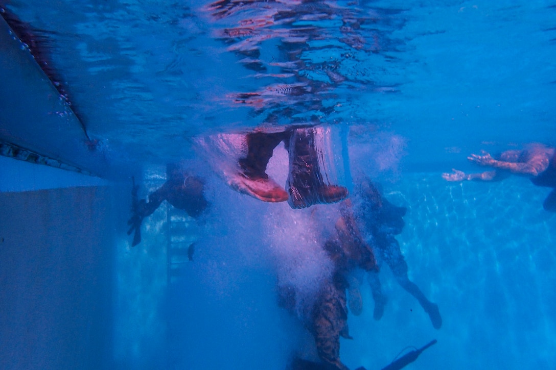 A Marine's boots and pant legs are visible underwater during a jump into a pool.