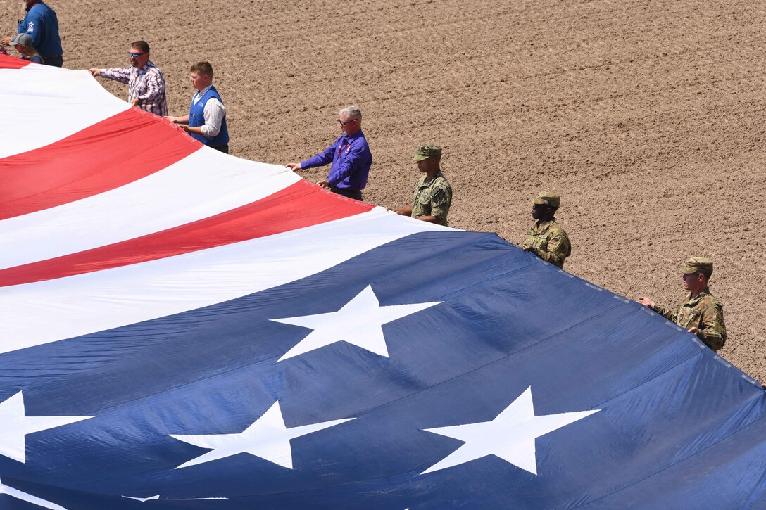 Service members and civilians unfurl the American flag across a park.