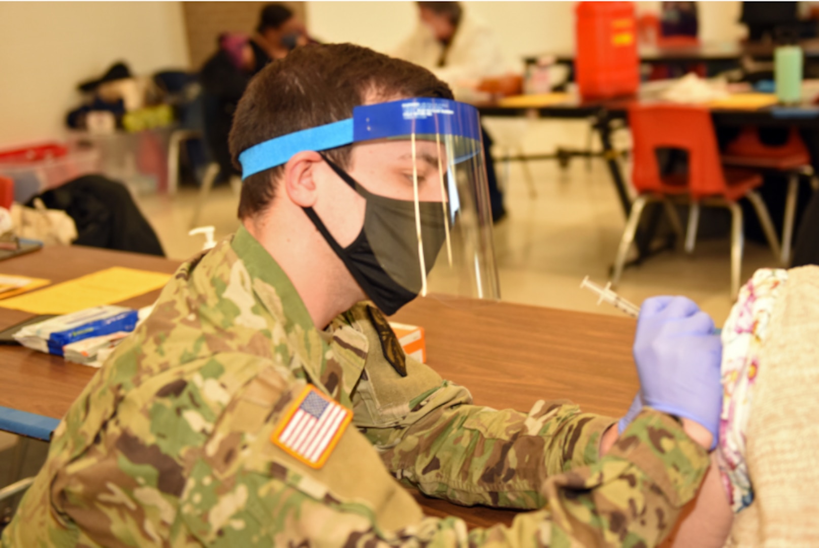 Photo By Master Sgt. David Kujawa | U.S. Army Spc. Kristopher Huffa, a medic with the Michigan Army National Guard, currently serving with Michigan National Guard’s (MING) Task Force Red Lion COVID-19 Vaccination/Testing Team (CVTT), administers the COVID-19 vaccine to members of the community for the Genesee County Health Department, held at the Flushing High School, Flint, Michigan, Feb. 20, 2021. MING COVID-19 vaccination testing teams are augmenting with local health care organizations, as requested, in the delivery and administration of the vaccination to Michiganders. (U.S. Air National Guard photo by Master Sgt. David Kujawa)