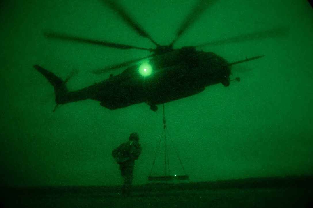 A Marine looks at a beam that is hooked to a helicopter as seen through night vision lens.