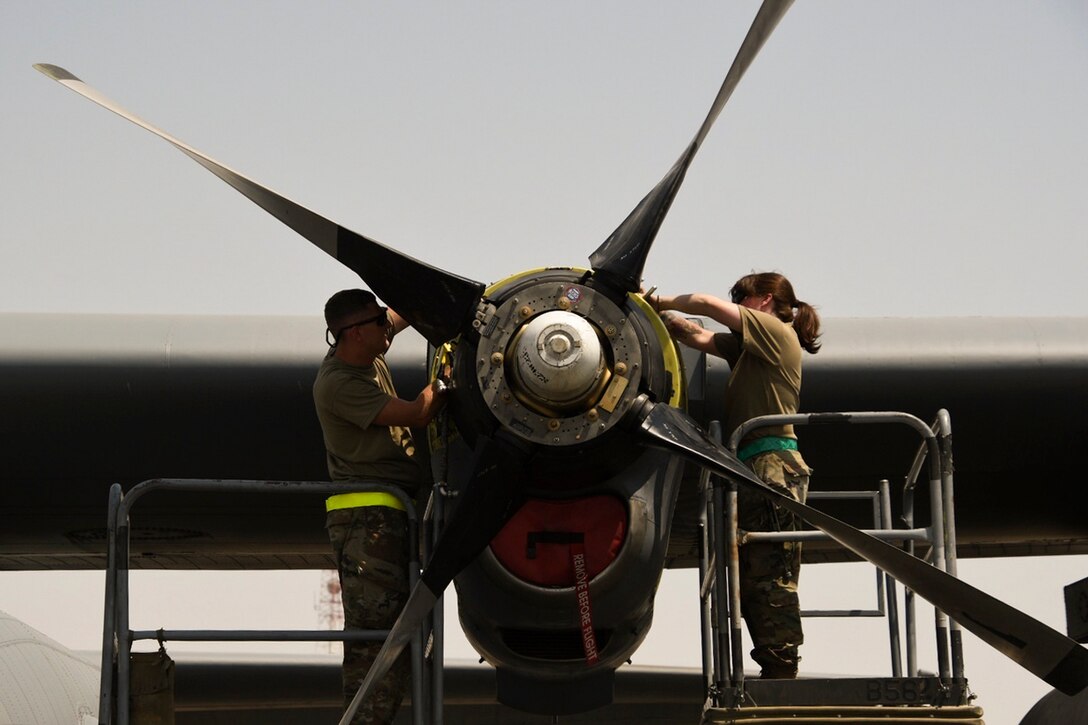 Two airmen change a propeller on an aircraft.