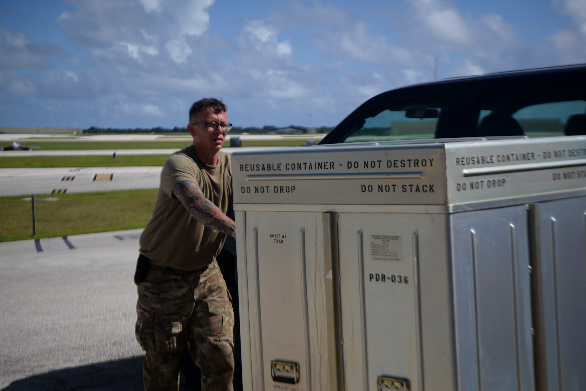 Airman pushes metal boxes full of equipment on a cart.