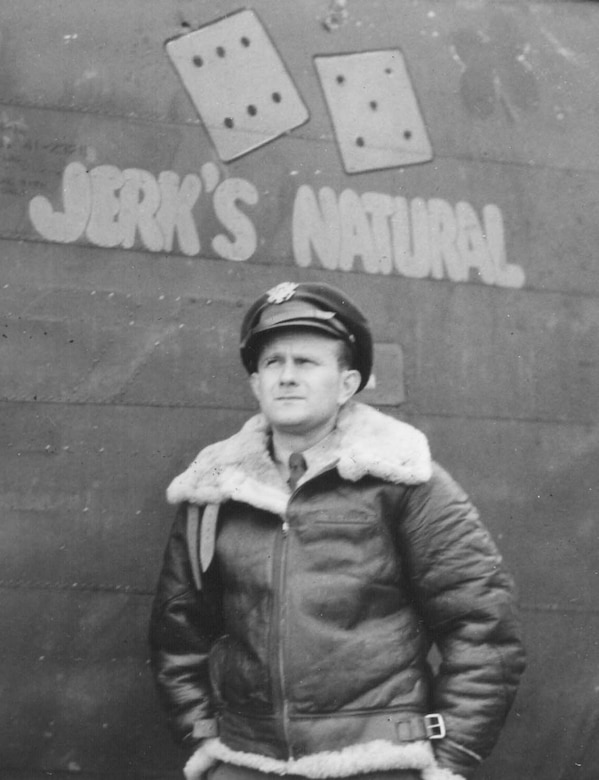 A man in a heavy jacket stands beside an airplane with two dice and "Jerk's Natural" stenciled on it.